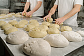 Cropped unrecognizable bakers forming bread from dough at table with flour and bowl in bakery