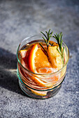 Summer tropical cocktail of vodka and sprite with ripe fruits and rosemary on grey background