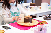 Crop faceless female confectioner in apron making delicious chocolate cake in circle shape