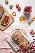 Top view composition of seeded whole grain bread arranged with honey jar of jam and walnut on table near knife