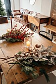 Festlicher Weihnachtsstrauß mit Baumwoll-, Tannen- und Eukalyptuszweigen und leuchtend roten Zweigen mit Beeren auf einem Holztisch mit Kerzen im Raum von oben