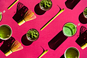 Top view full frame bright background of glass of green tea and dried matcha with bamboo chasen and chashaku on pink surface