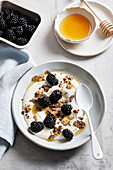 Von oben köstliches Frühstück mit Joghurt mit frischen Brombeeren, Honig und Müsli auf einem Marmortisch in der Küche