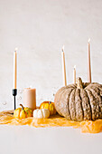 Burning candles in sticks and assorted pumpkins arrange on white table during Halloween celebration