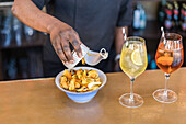 Focused African American female bartender serving tasty mussels snacks in can on counter with alcohol cocktails in bar