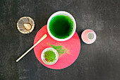 Top view of healthy matcha tea and dried powder near wooden chasen and chashaku on bright round stand on black table at sunlight