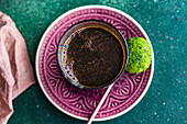 Blick von oben auf ein Glas türkischen Kaffee und traditionelle süße Pakhlava-Kugeln, serviert auf einem grünen Betontisch