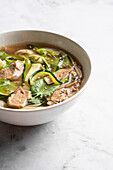 Bowl of traditional Vietnamese Pho bo noodle soup with basil leaves and lime placed on marble table in light room