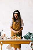 Concentrated female floral designer in apron standing at table and creating floral composition with blooming roses in workshop
