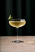 Elegant crystal coupe glass of champagne cocktail decorated with lime slice served on marble counter in restaurant