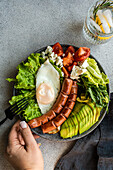 healthy ketogenic lunch plate with vegetables, fried egg and sausages served on the concrete plate