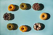 Circle of donuts of different colors and flavors with copy space in the center on blue background