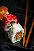 Top view composition of delicious fresh various sushi and bamboo chopsticks served on black platter on checkered cloth