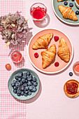 From above of composition of plated with fresh baked sweet croissants served with berries and jam placed on pink table