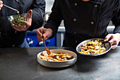 Anonymous male and female chefs arranging ingredients on bowl while preparing tasty dish in contemporary restaurant kitchen together