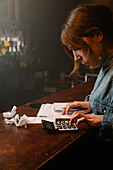 Side view of focused female worker using calculator to count income while sitting at counter with documents during work in cafe