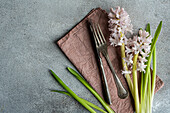 From above spring table setting with hyacinth flower near cutlery on grey concrete table for festive dinner