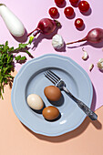 Top view of chicken eggs on plate with fork against fresh parsley sprigs and cherry tomatoes on two color background