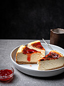 Plate with sliced delicious homemade cheesecake and jar with sweet jam placed on gray table
