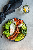 healthy ketogenic lunch plate with vegetables, fried egg and sausages served on the concrete plate