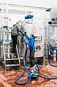 Side view of male coworkers in face masks connecting hose to metal reservoir in beer factory during coronavirus pandemic