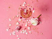 Draufsicht auf eine Komposition mit rosafarbenem Mocktail, verziert mit Rosenblättern und einer blühenden Blume auf einer hellen Fläche