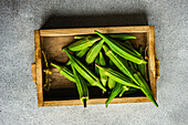 From above raw and fresh bamia vegetables in wooden tray box on concrete background