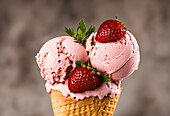 Delicious ice cream scoops with strawberry slices and mint leaves in waffle cone on blurred background
