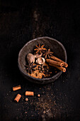 From above of wooden bowl with aromatic cinnamon sticks and anise stars with nutmeg and cloves placed on dark table