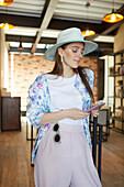 Smiling young female in stylish apparel with cellphone in cafeteria with lamps