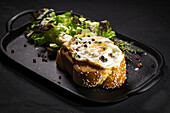 Fried egg on brioche served on tray with fresh lettuce for appetizing breakfast on black background