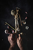 From above cropped unrecognizable person hands arranging bouquet of fresh purple garlic cloves placed in dark background