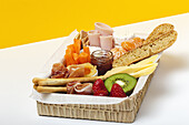 Brunch box with assorted sliced meats various types of cheese and crispbreads arranged near ripe cup kiwi sweet strawberries and peeled mandarin near jam in glass jar on colorful background