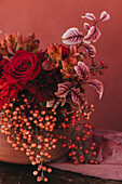 Ausschnitt eines eleganten Blumenstraußes aus frischen, üppigen roten Rosen und Lilien mit Zweigen roter Beeren, die in der Nähe des Stoffes platziert sind