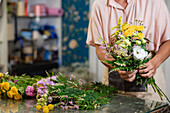 Crop faceless female florist creating flower bouquet while working at table in floral store