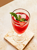 From above of tasty refreshing red beverage with ice cubes and aromatic mint leaves in glass on coaster