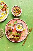 Top view of plate with delicious cream cheese and assorted vegetables placed on napkin near vegan fritters on green background