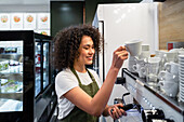 Side view barista with portafilter and cup preparing aromatic drink in coffee machine in cafe