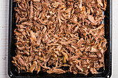 Top view of pile of cooked pulled meat on small fibers and pieces covering baking pan while preparing Cuban bowl