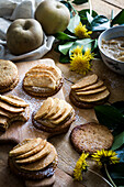 Süße Kekse mit Apfelscheiben auf dem Tisch und Schneidebrett neben Löwenzahn
