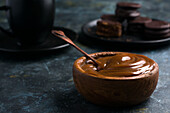 Dulce de leche in brown bowl against black cup and saucer near chocolate alfajores