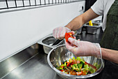 Crop male seller in uniform standing at counter in salad bar and cutting vegetables while preparing healthy food