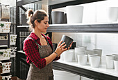 Side view of adult woman in apron arranging empty pots on shelf while working in flower store