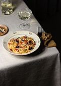 Spaghetti alla Puttanesca server with glass oh white wine placed on table with napkin