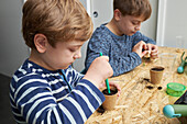 Siblings planting seedling in cardboard cup with ground at table with gardening shovel