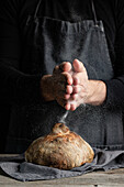 Unbekannter Koch in Schürze steht am Tisch und verziert einen Laib traditionelles Brot mit Mehl