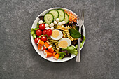 Gesunder Salat mit verschiedenen Gemüsesorten und Nudeln mit gekochten Eiern und Grünzeug in einer Schüssel mit Gabel auf einem Steintisch serviert