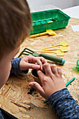 Crop anonymous kid planting seedling in cardboard cup with ground at table with gardening shovel
