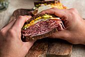 From above of crop anonymous client of restaurant eating tasty sandwich made with bacon toasts and lettuce leaves with water with lime