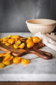 Pile of fresh orange cut kumquats on wooden chopping board placed on marble table with towel in kitchen